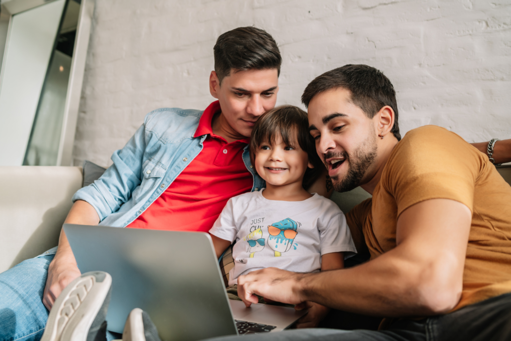 Two dads with child and computer, smiling.